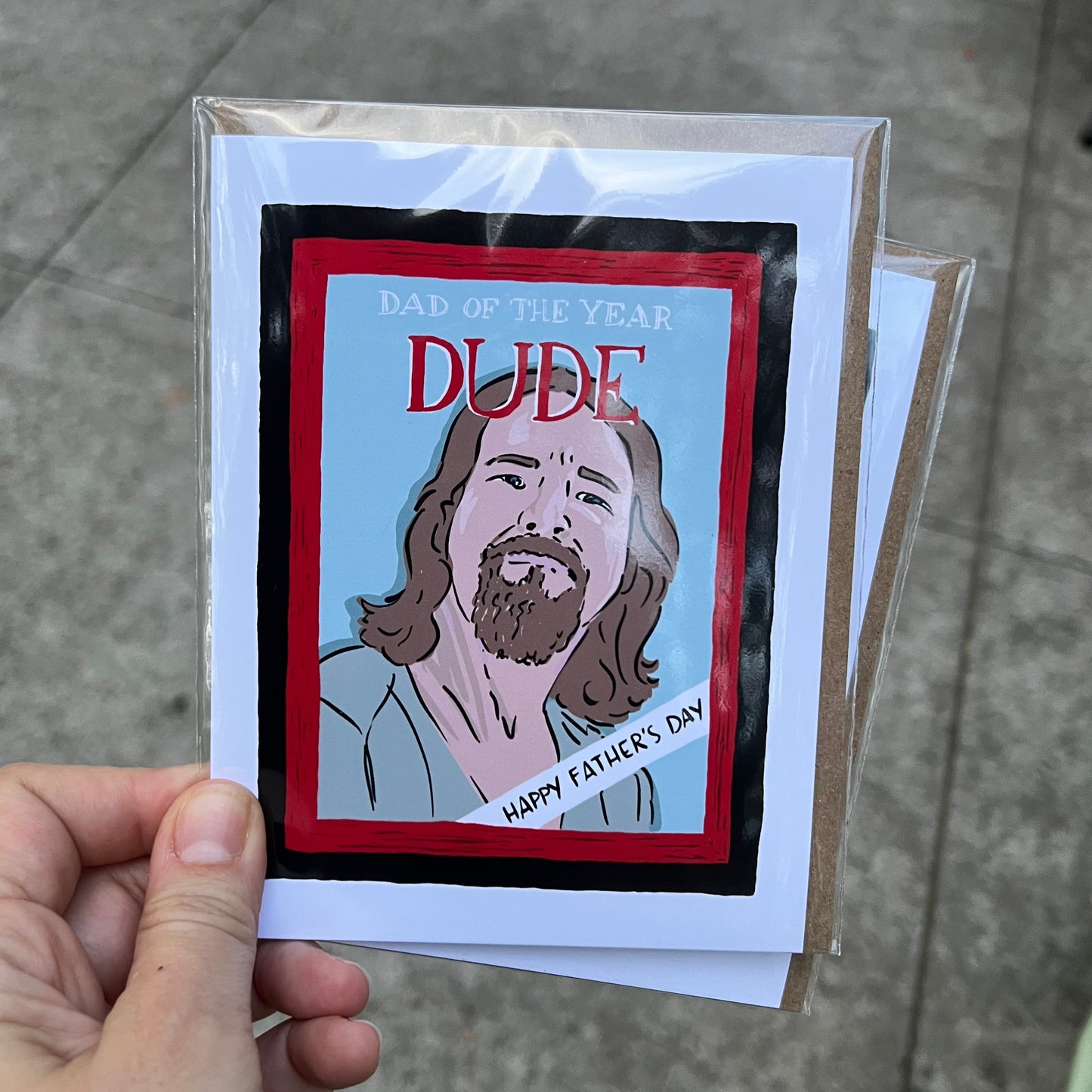 Hand holding a card with a graphic design of a person and text, on a concrete surface.