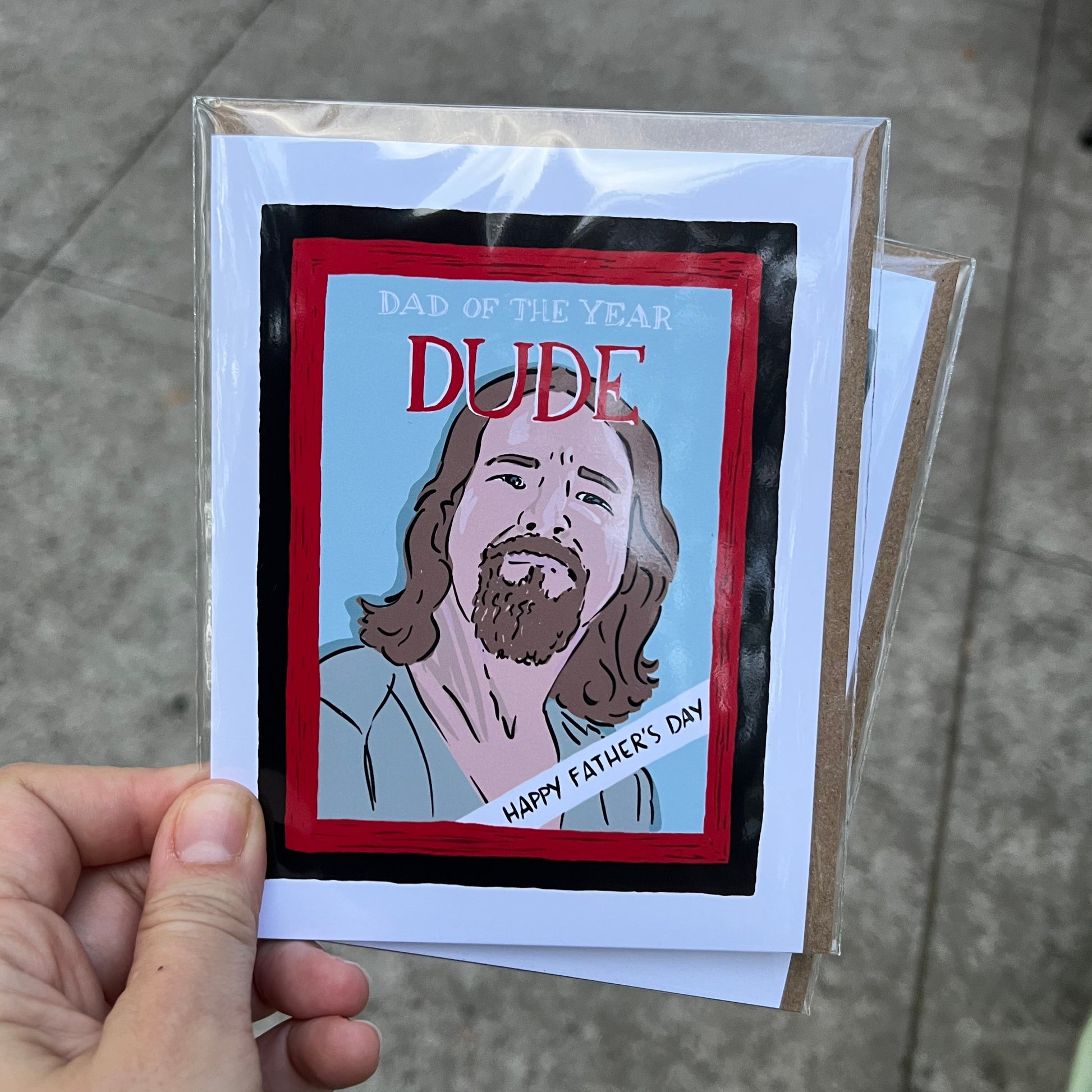 Hand holding a card with a graphic design of a person and text, on a concrete surface.