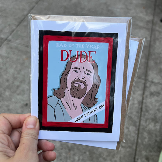 Hand holding a card with a graphic design of a person and text, on a concrete surface.
