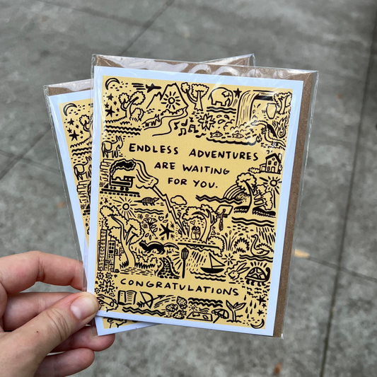 Hand holding a card with gold text and illustrations on a gray pavement background