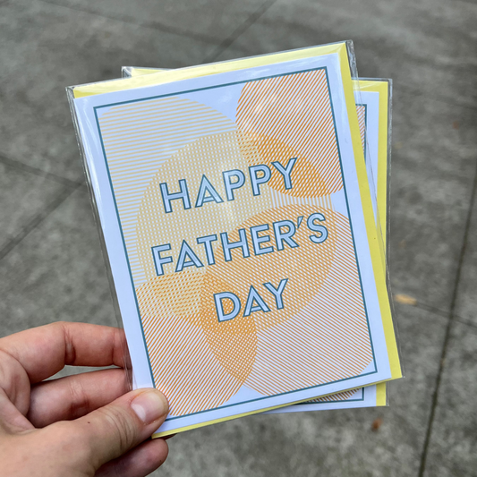 Hand holding a 'Happy Father's Day' card on a pavement background